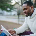 man wearing white sweater while reading book